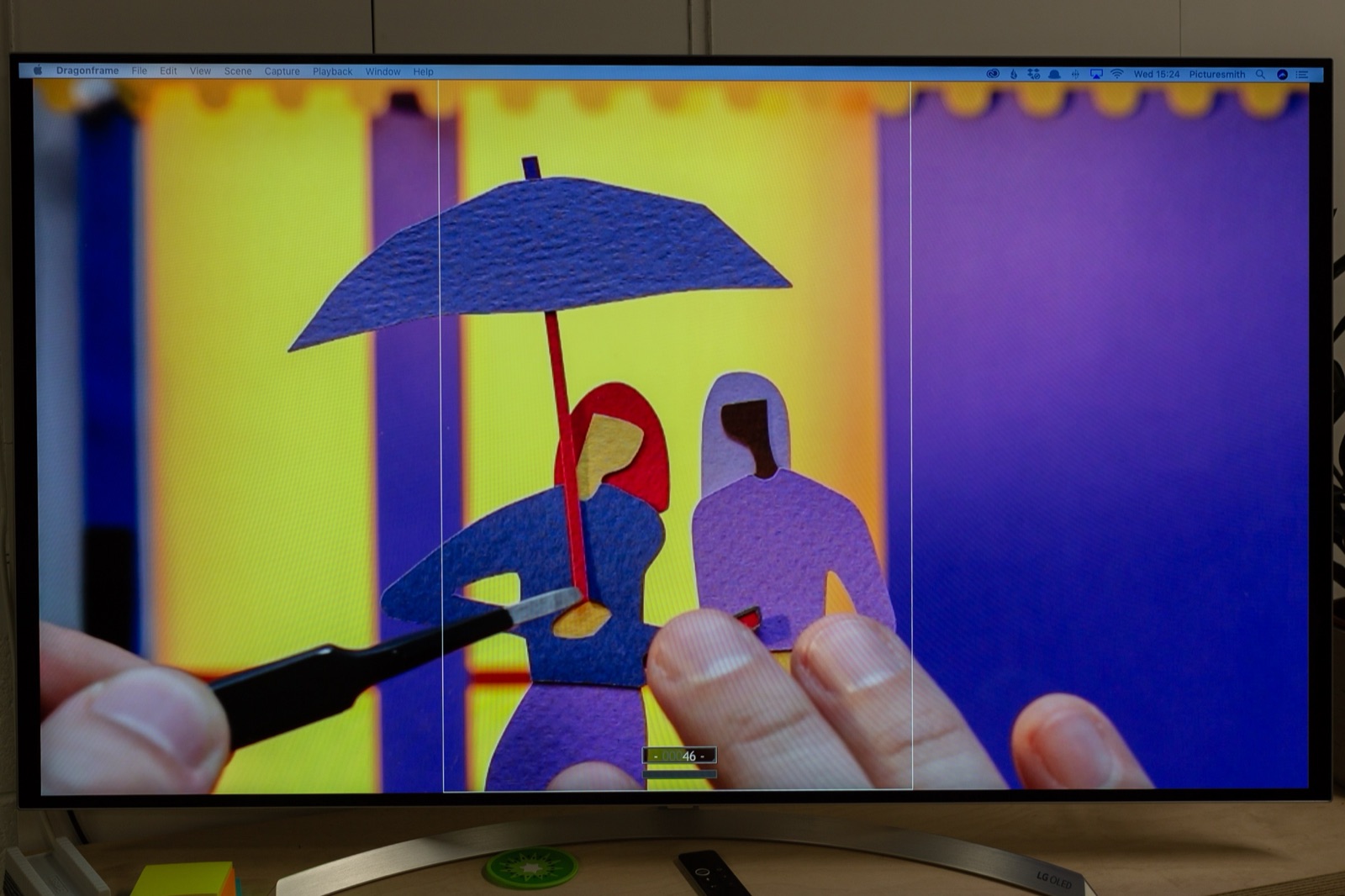 Animating on the multi-plane — fingers carefully positioning a paper character against the monitor showing the live camera feed