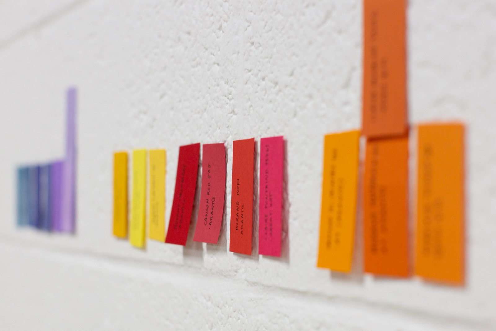 Colour palette reference pinned to the studio wall — paper swatches running from purple through red, yellow and orange